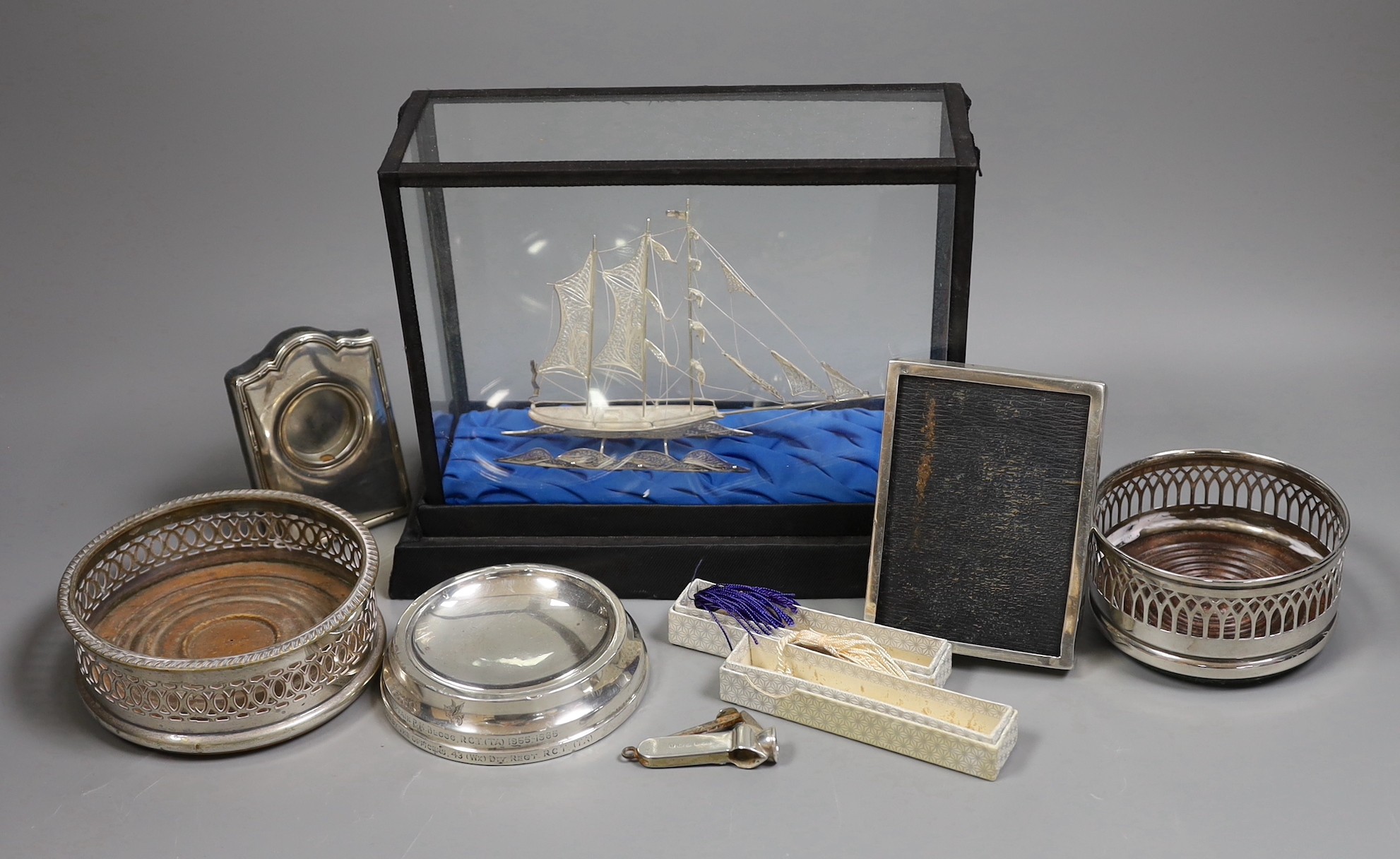A group of silver and white metal items including a cased boat model, cigar cutter and mounted photograph frame and plated items